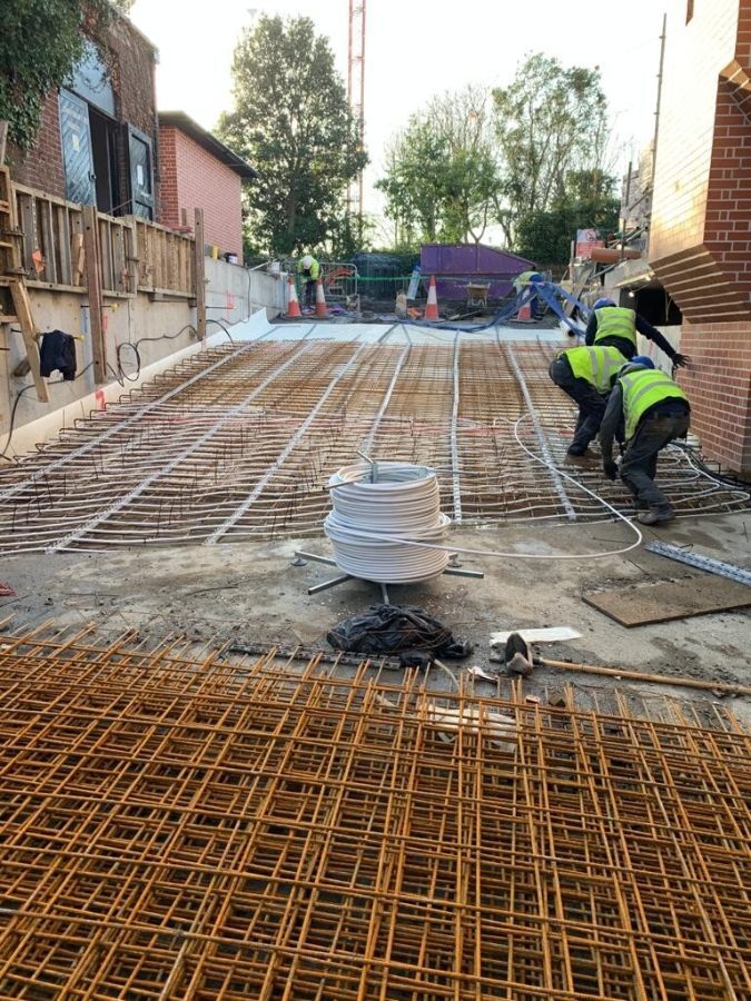 Groundworks crew laying underfloor pipework over steel reinforcement
